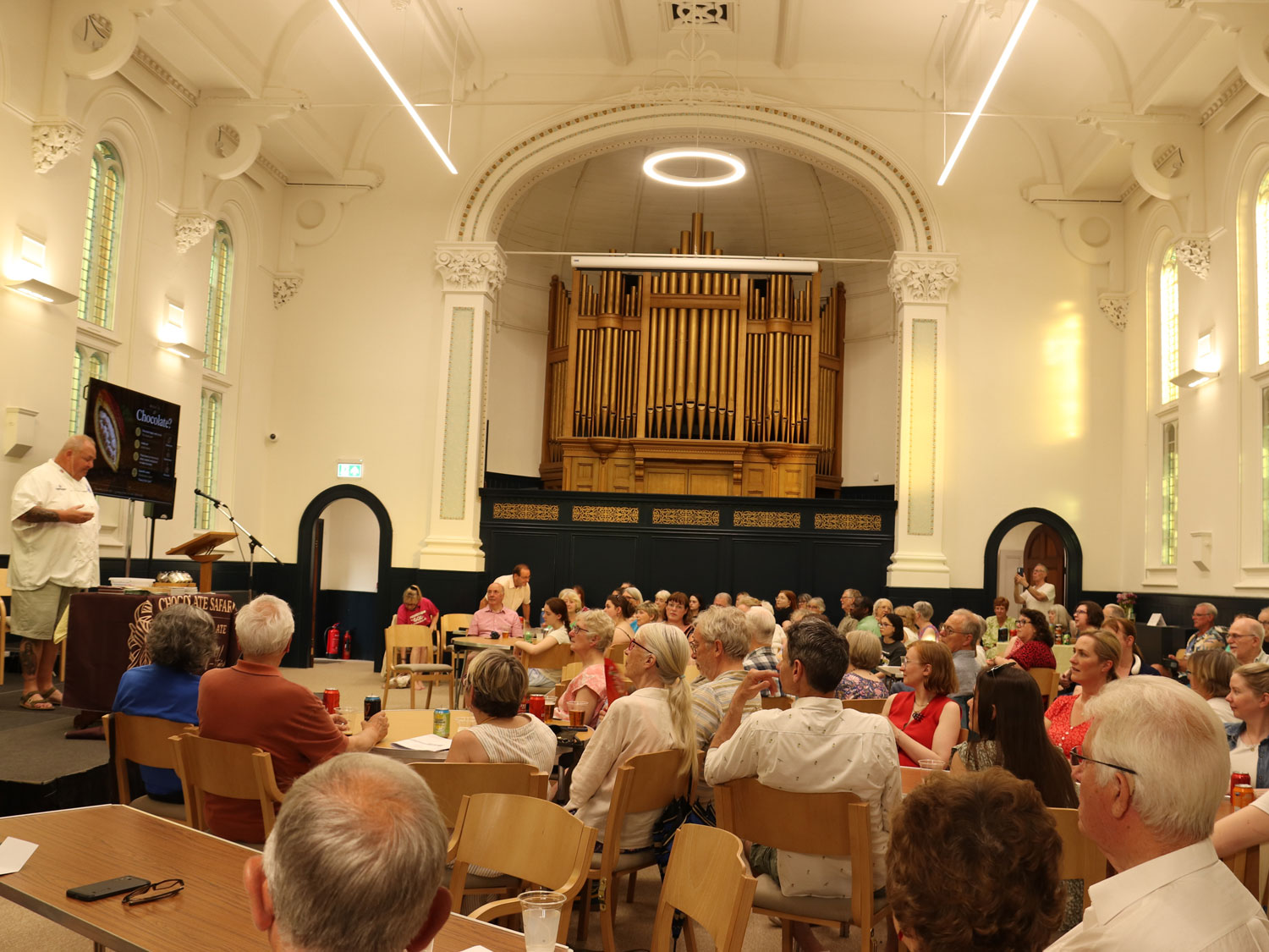 Trinity Hall at The Link Centre with people sitting at tables looking at someone on stage talking about chocolate.
